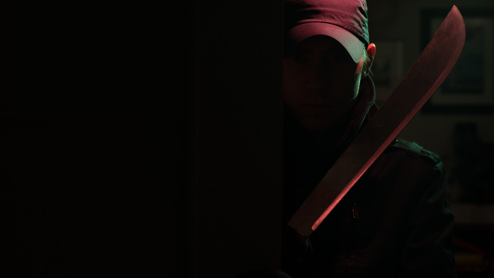 Image of killer with machete in dark apartment with red light at night