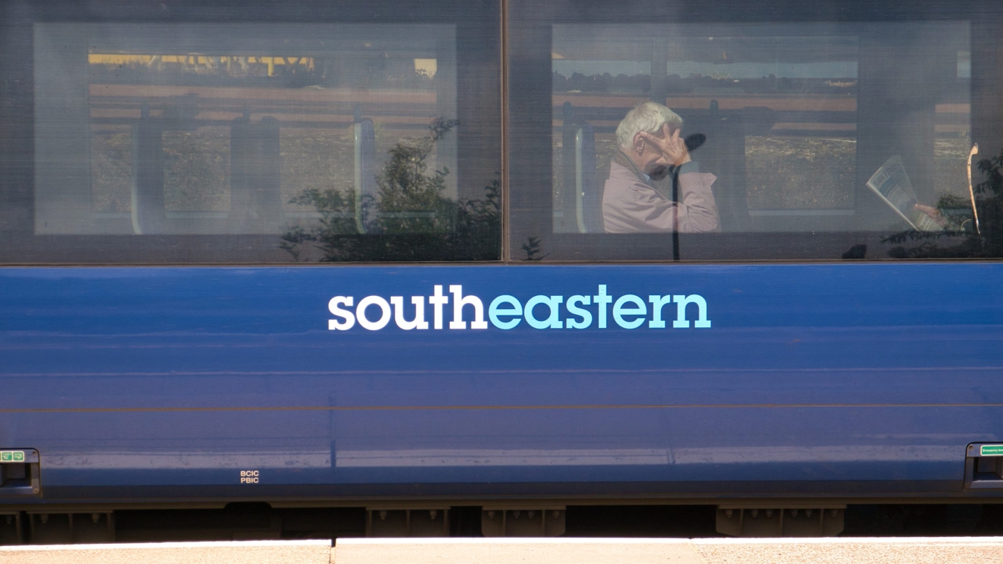 The side of a blue southeastern Railways carriage. Behind one of the two windows, commuters sit waiting for the train to continue its journey.