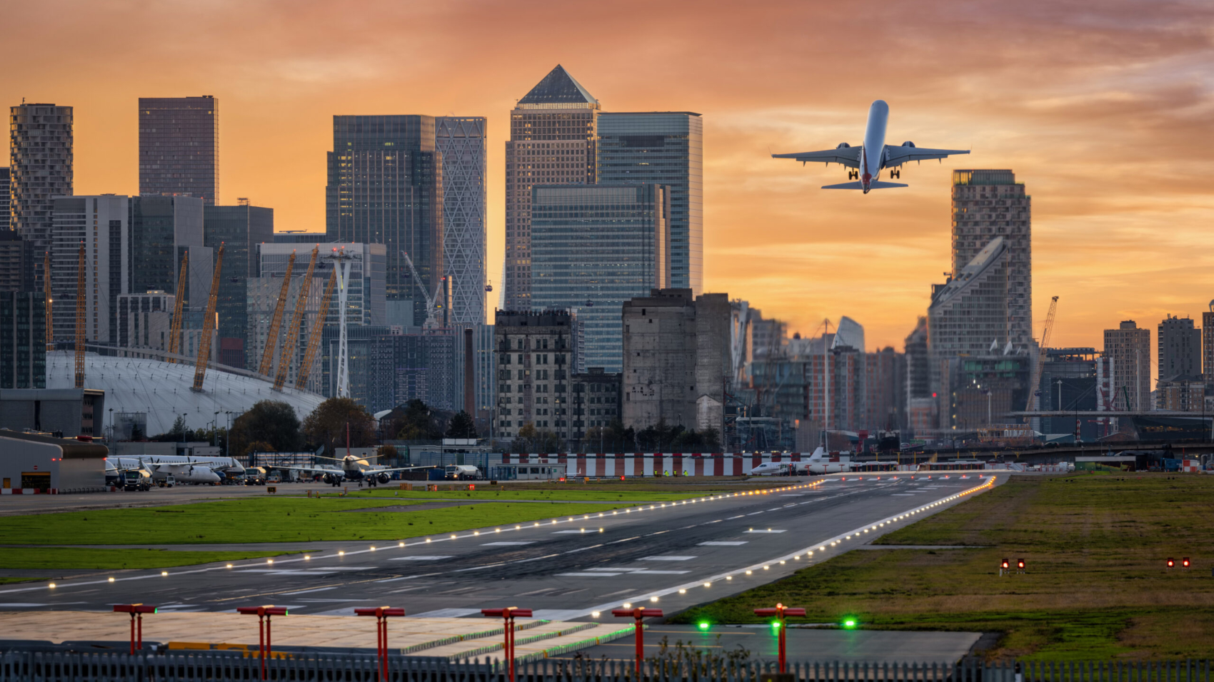 Panoramic view of the London skyline with Canary Wharf district and the runway of the City Airport in front during sunset time